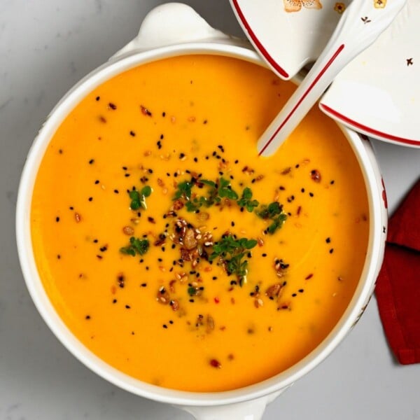 Bowl of creamy butternut squash soup, garnished with toasted seeds and fresh herbs.