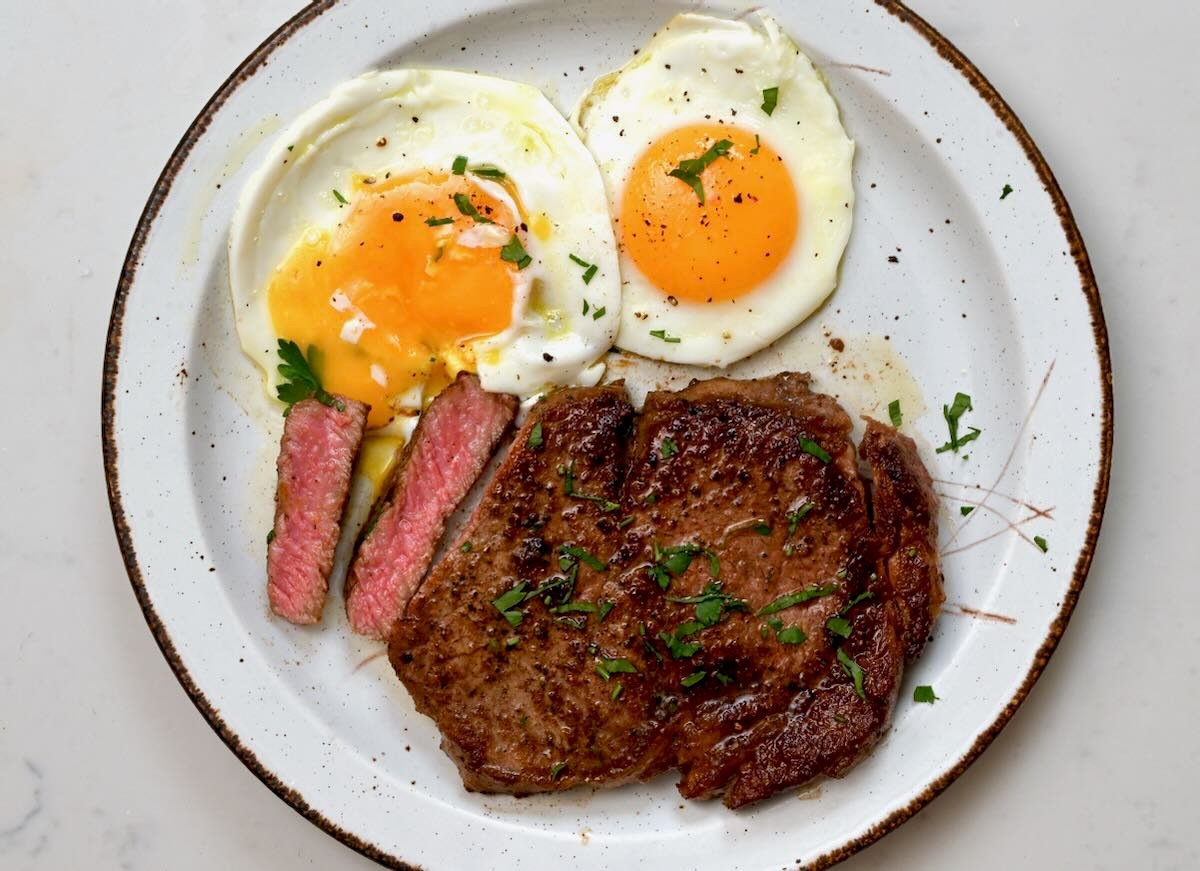 A seving of steak and sunny-side-up eggs topped with a bit of parsley. - 6
