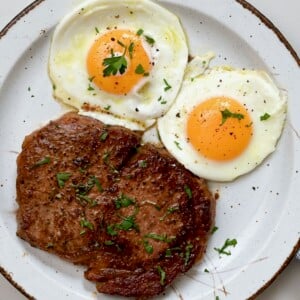 A seving of steak and sunny-side-up eggs topped with a bit of parsley. - 18