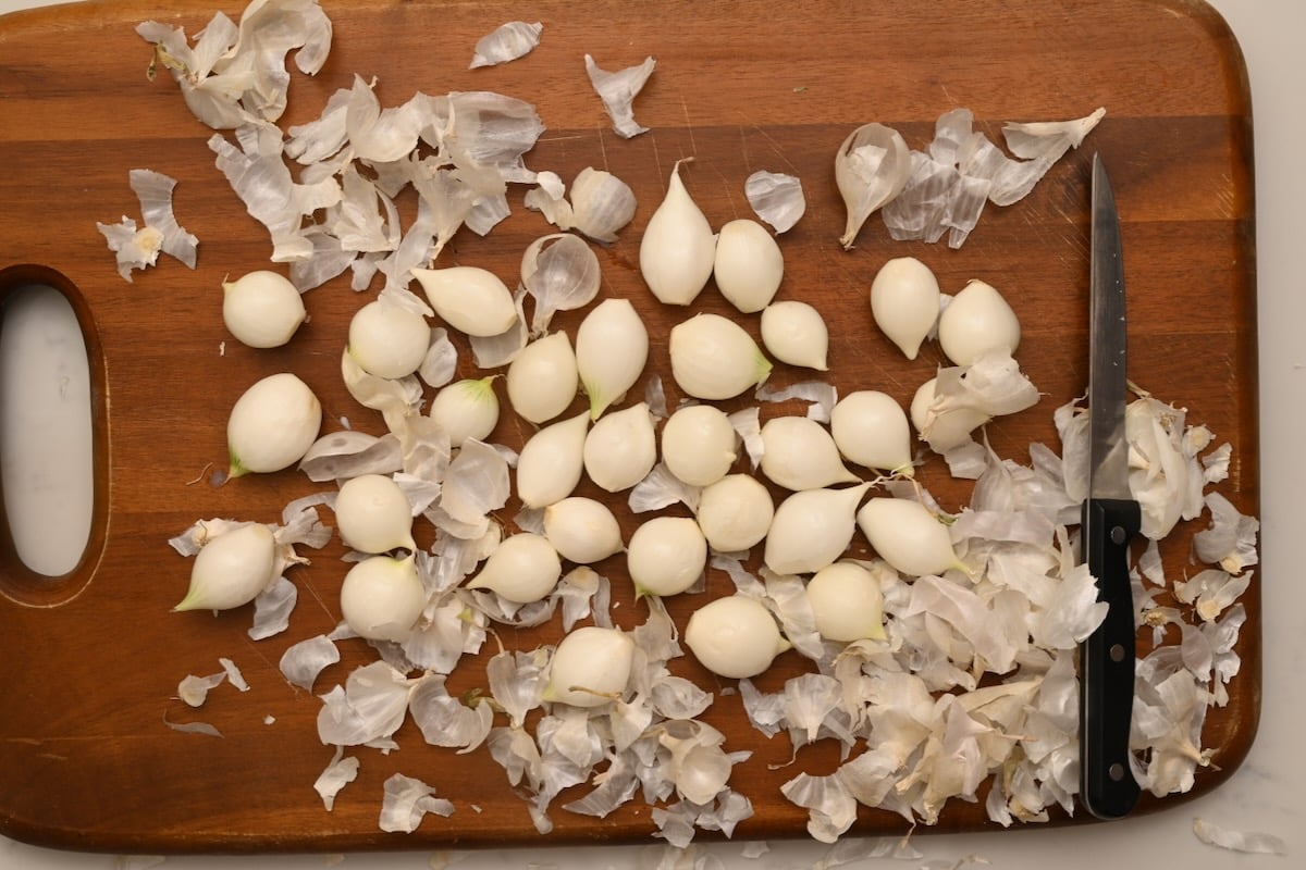 Peeled pearl onions on a wooden board with their skins scattered around, prepared for beef bourguignon. - 4