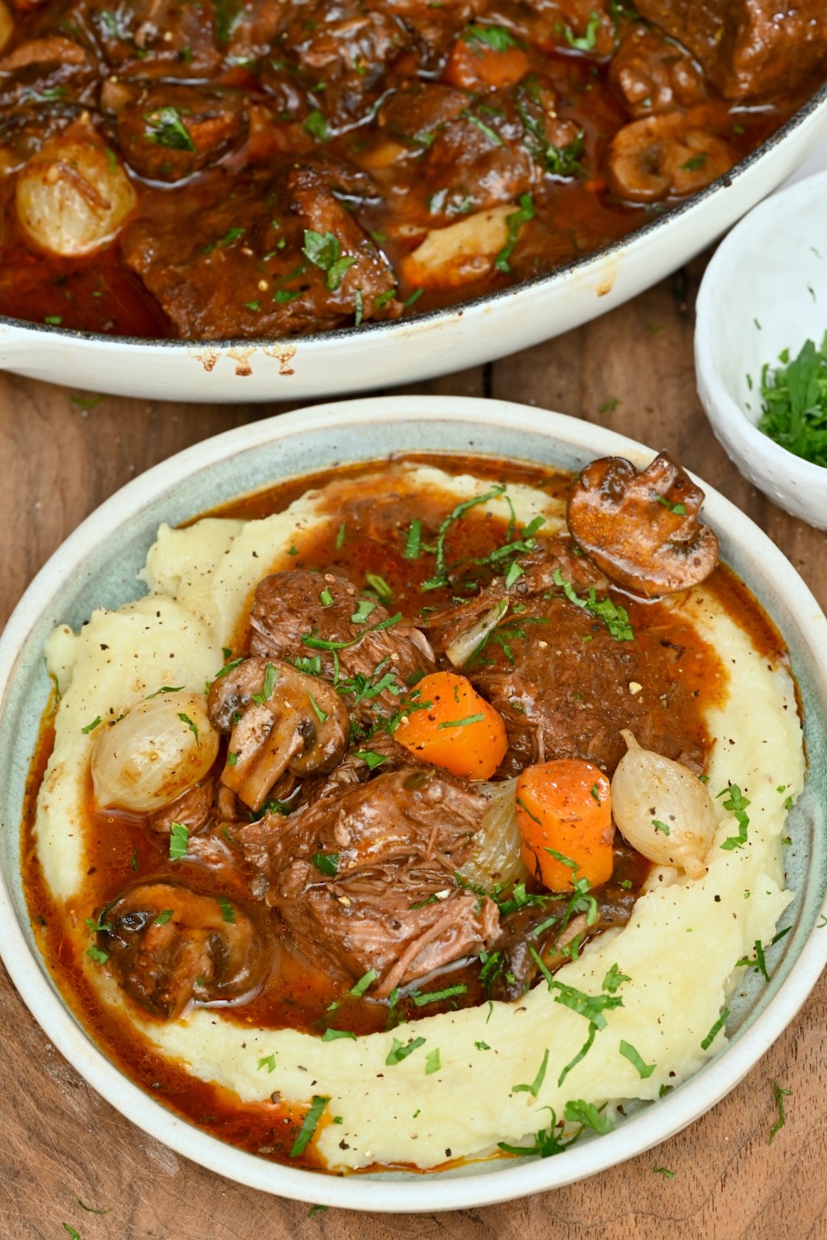 A bowl of beef bourguignon served over creamy mashed potatoes with tender beef, carrots, mushrooms, and pearl onions. - 25