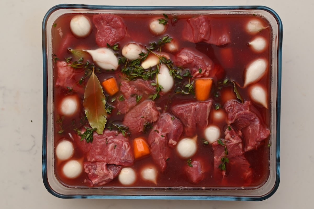 Beef bourguignon ingredients marinating in red wine with pearl onions, carrots, thyme, and bay leaves. - 7