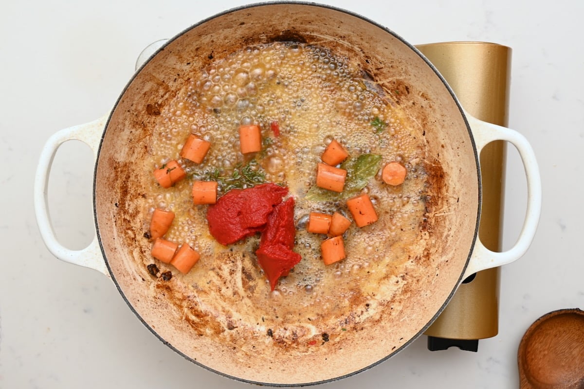 Tomato paste simmering with carrots and herbs to build the flavor base for beef bourguignon. - 18