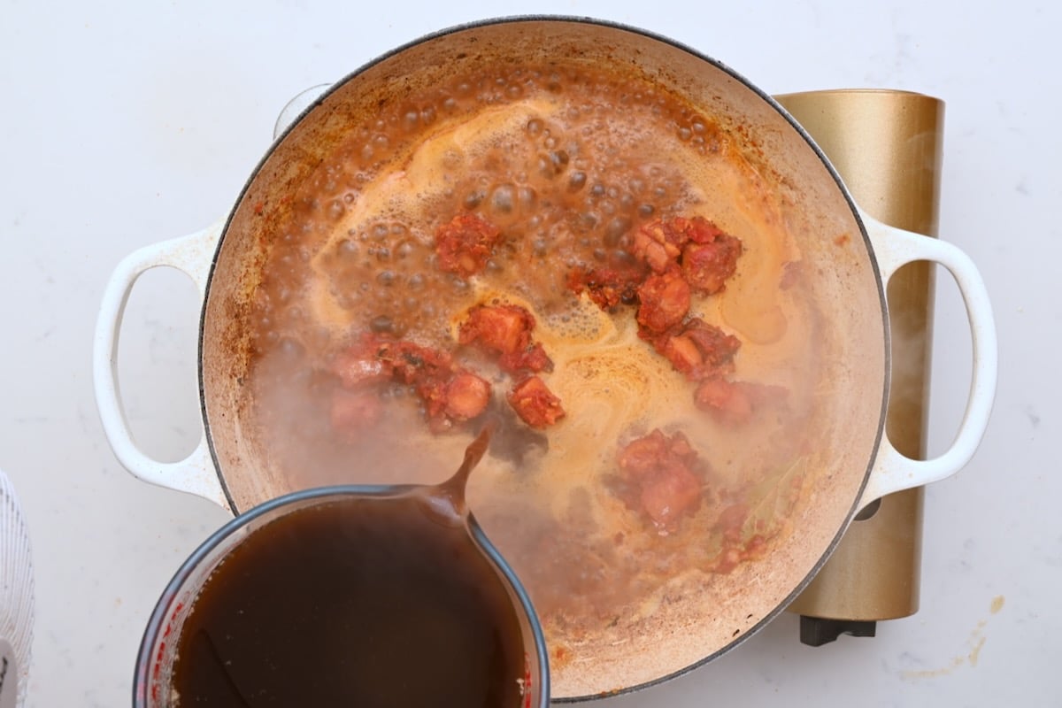 Hot beef stock being poured into the pot to build the sauce for beef bourguignon. - 19