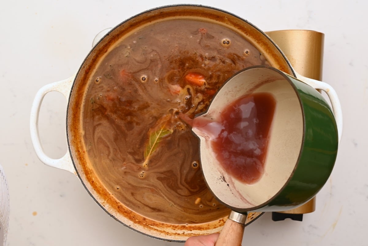 Reduced red wine being poured into the pot to deepen the flavor of beef bourguignon. - 22