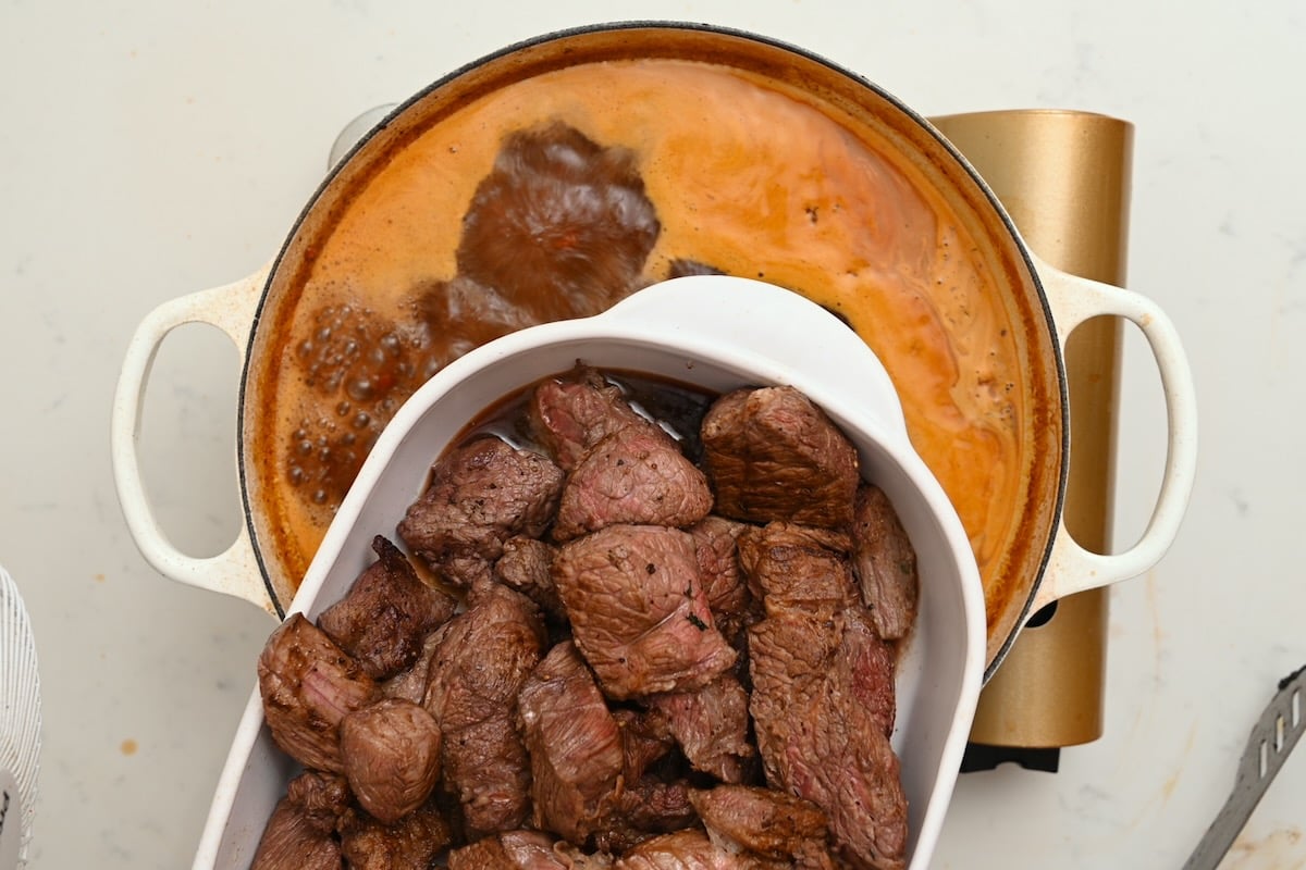Seared beef pieces being added back into the simmering sauce for beef bourguignon. - 20