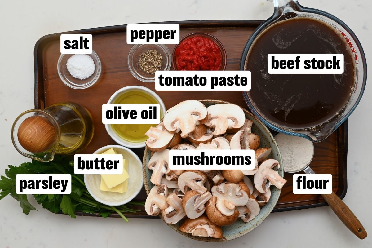 Mushrooms, beef stock, tomato paste, butter, olive oil, flour, parsley, salt, and pepper arranged on a counter. - 3