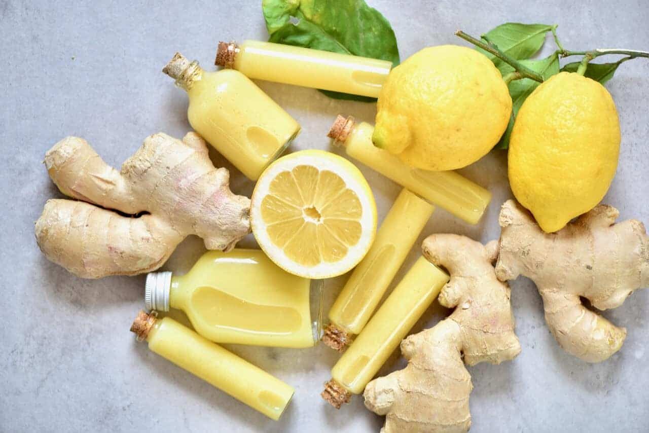 Fresh ginger lemon shots in small vials with some ginger and lemons around them.