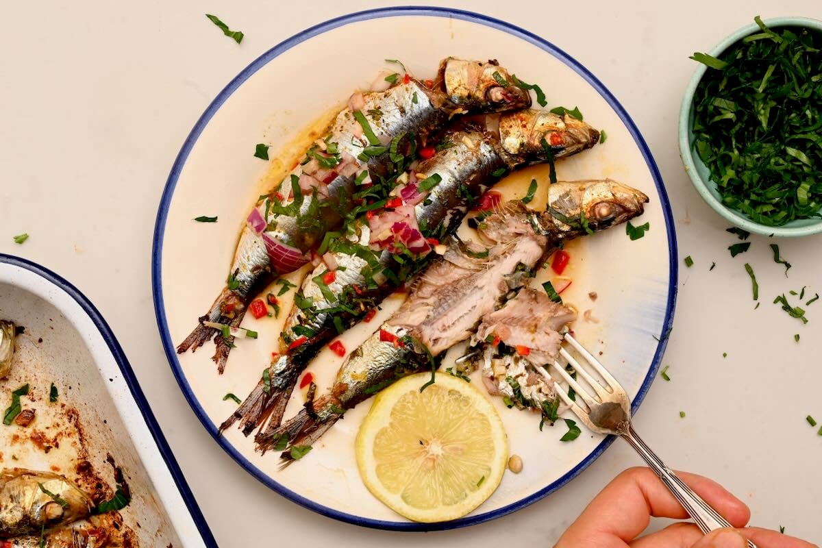 Three roasted sardines served on a plate with lemon slice. - 6