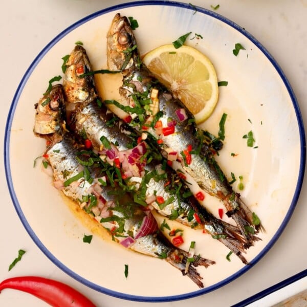 Three roasted sardines served on a plate with lemon slice.