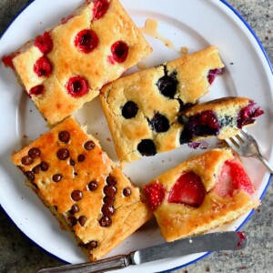 Sliced sheet pan pancakes with berries, chocolate chips, and drizzled with maple syrup.