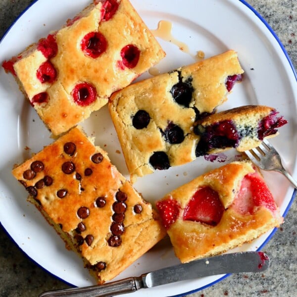 Sliced sheet pan pancakes with berries, chocolate chips, and drizzled with maple syrup.