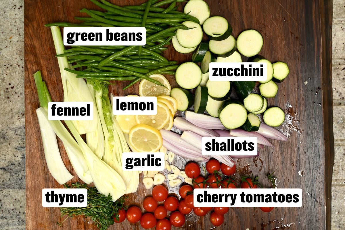 Vegetables and aromatics for baked mackerel on a wooden board, including zucchini, fennel, green beans, cherry tomatoes, lemon, garlic, shallots, and thyme. - 3