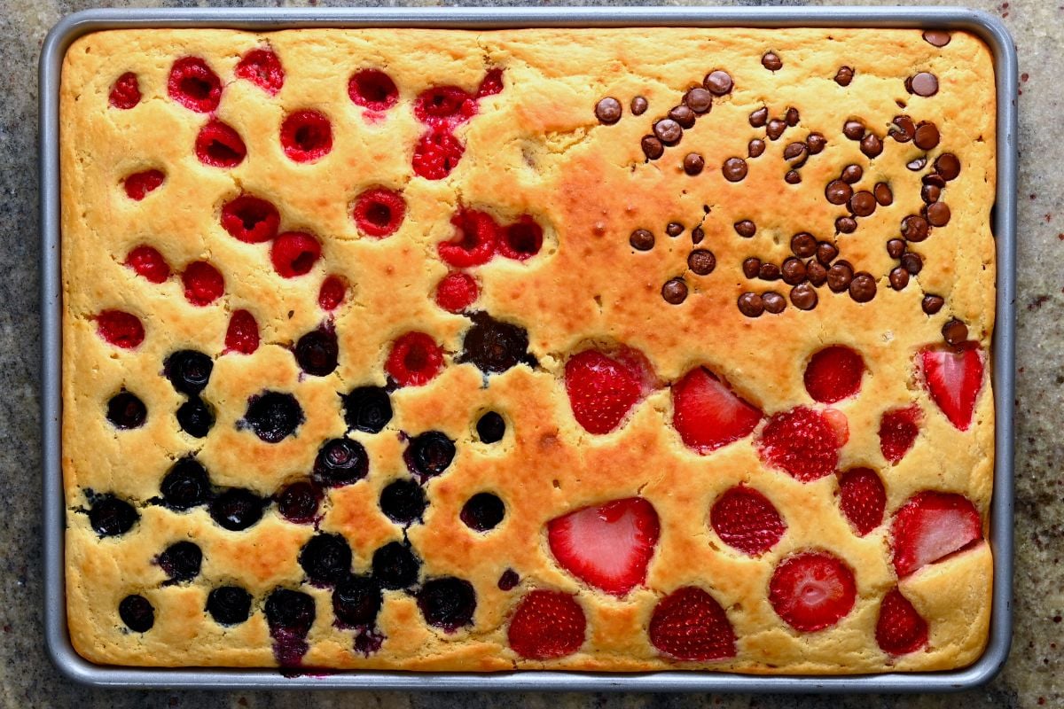 Baked sheet pan pancakes with golden batter topped with raspberries, blueberries, sliced strawberries, and chocolate chips. - 6