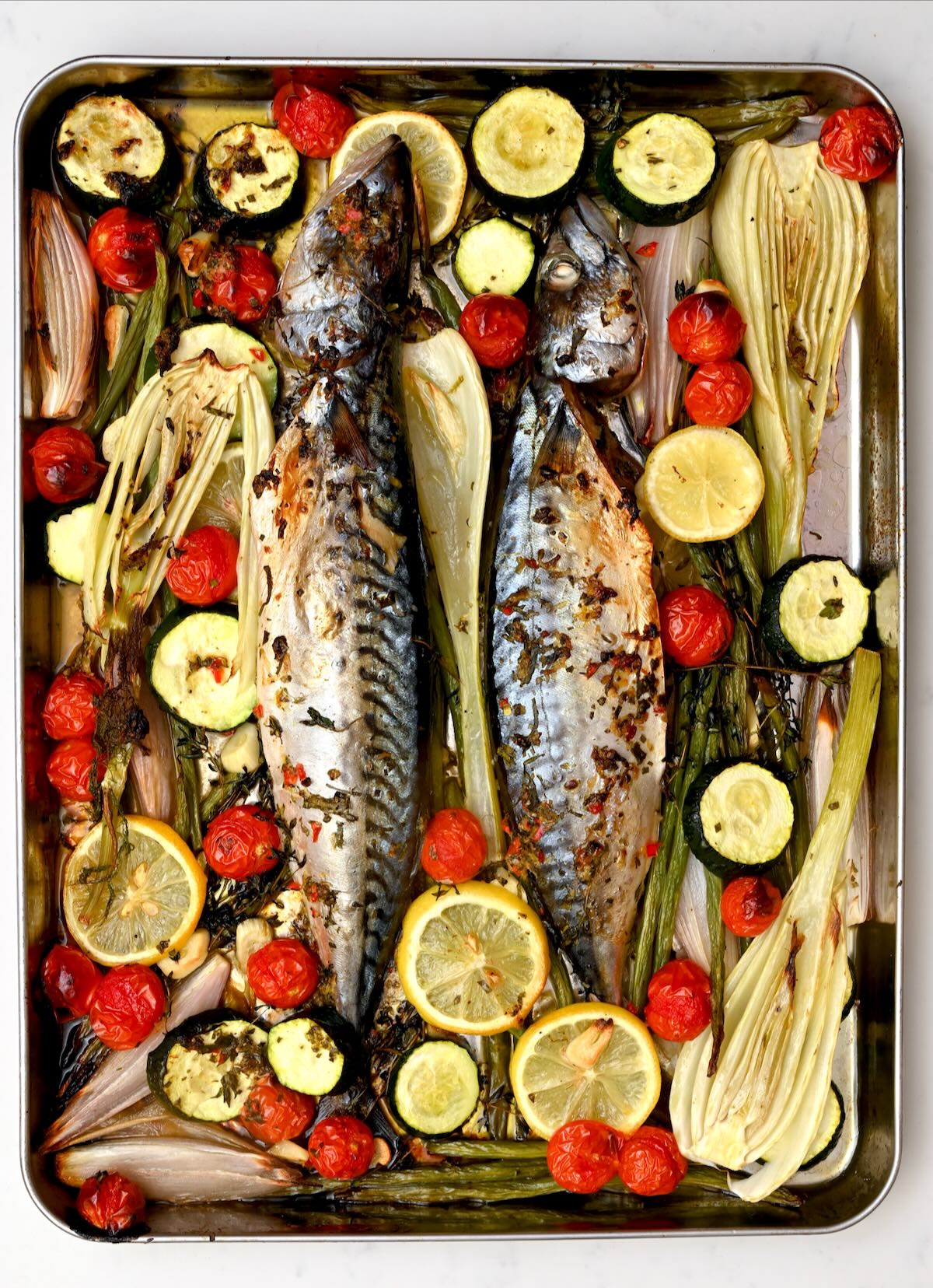 Whole oven-baked mackerel roasted on a sheet pan with fennel, zucchini, cherry tomatoes, lemon slices, and fresh herbs. - 1