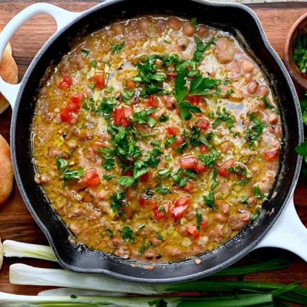 Ful medames in a skillet with parsley, tomatoes, and olive oil.