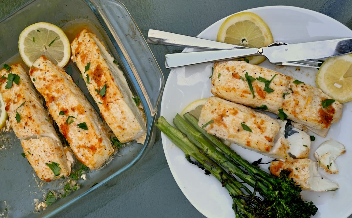 A serving of baked halibut fish with roasted broccolini and a few lemon slices.