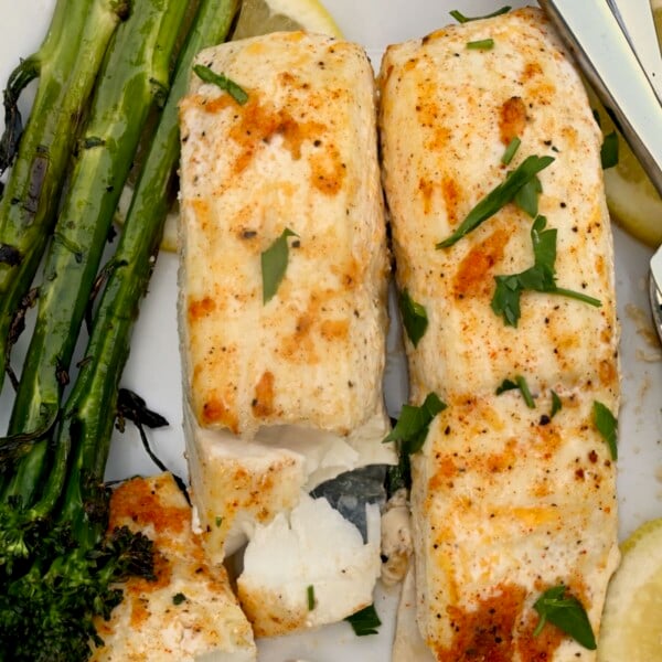 A serving of baked halibut fish with roasted broccolini and a few lemon slices.