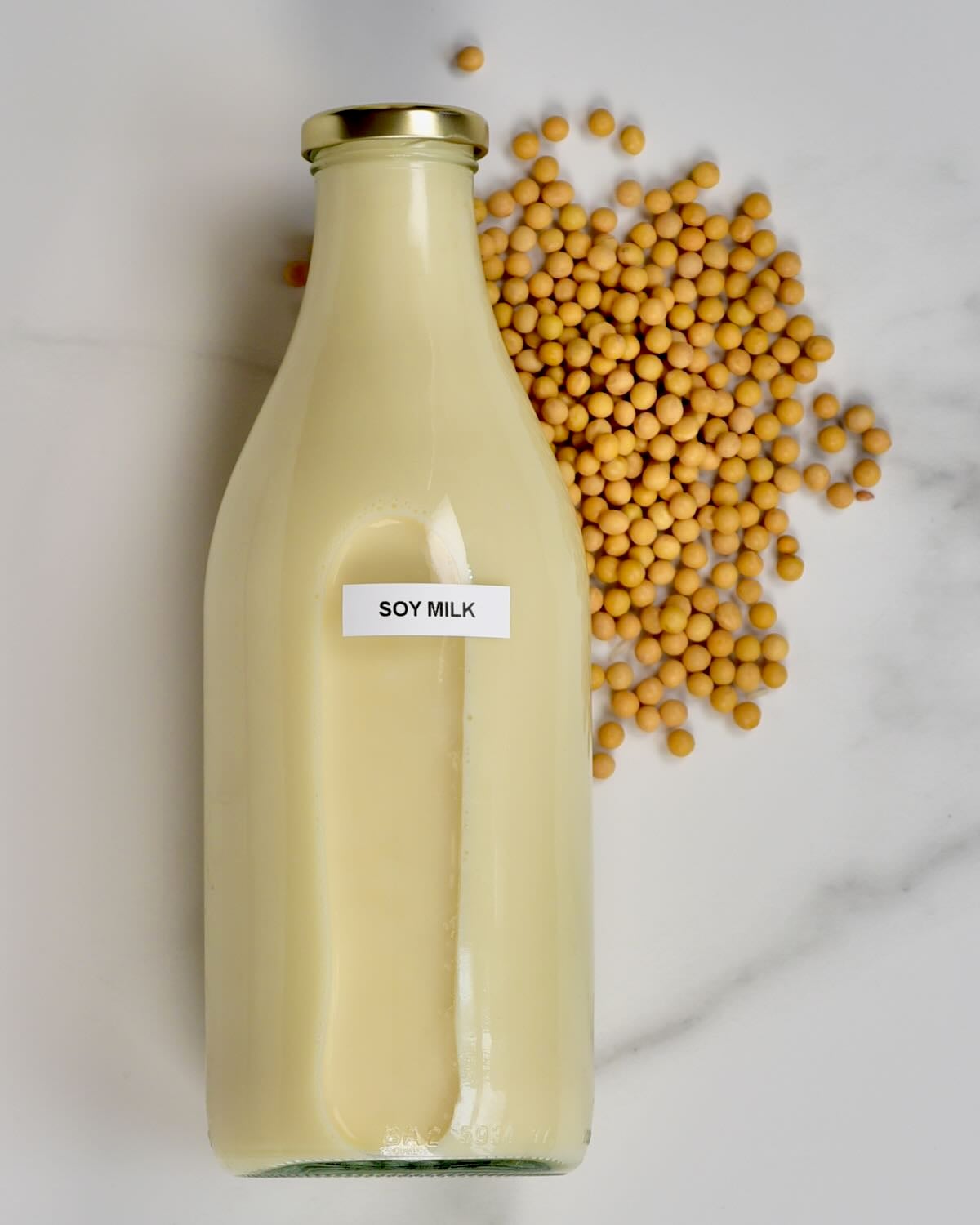 A bottle with homemade soy milk and some soybeans next to it.