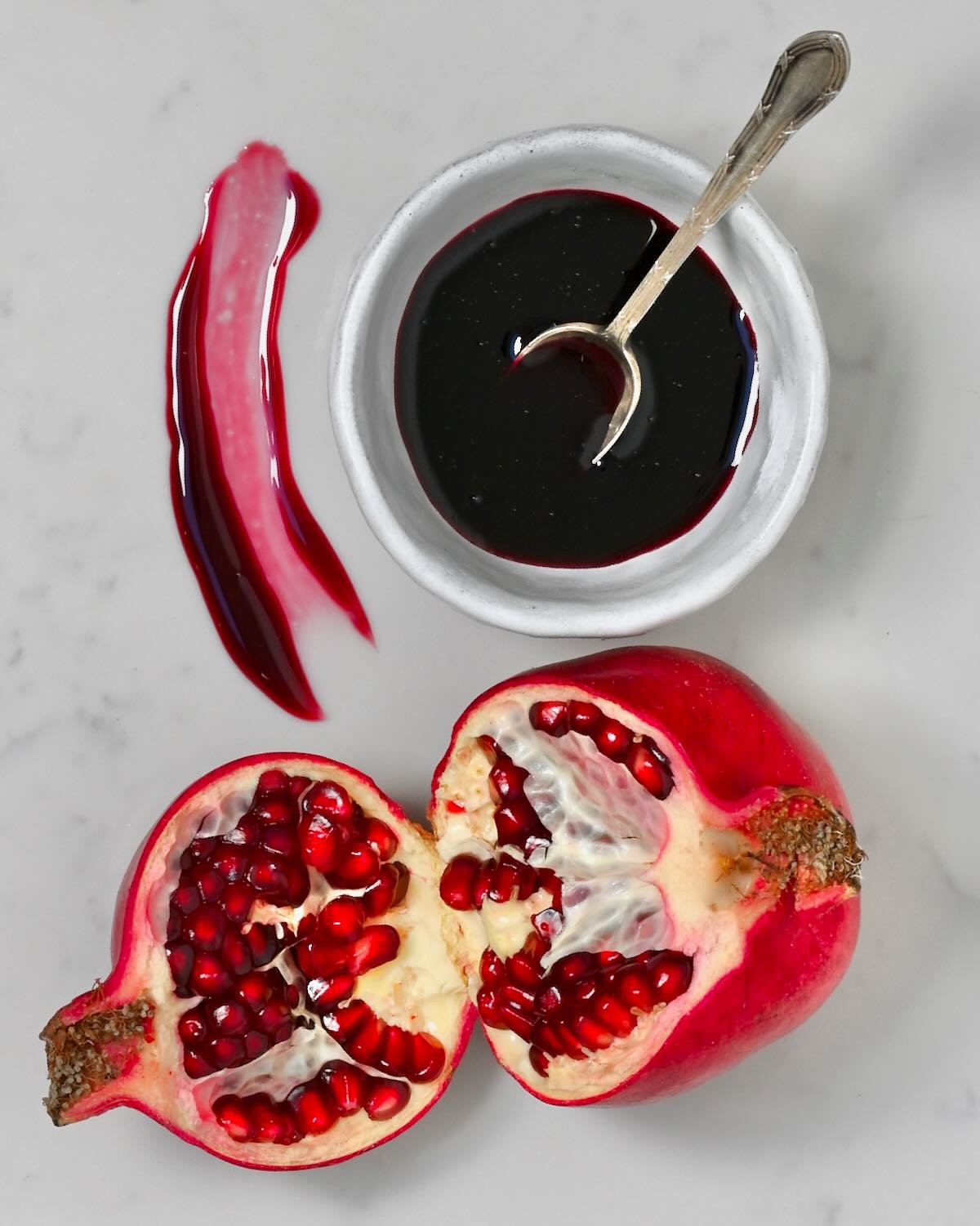 A small bowl with homemade pomegranate molasses and an opened pomegranate next to it. - 1