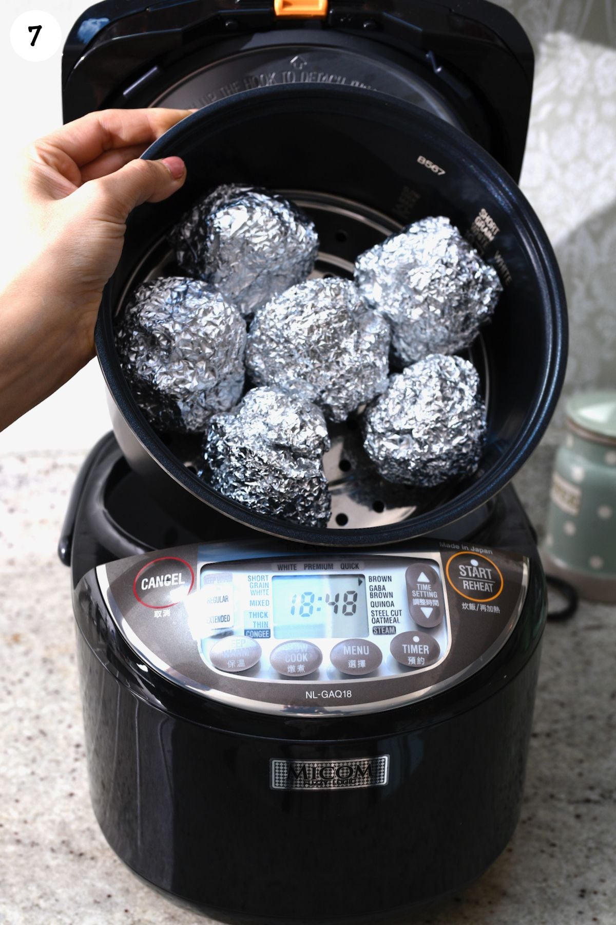 Placing wrapped garlic heads in a rice cooker.