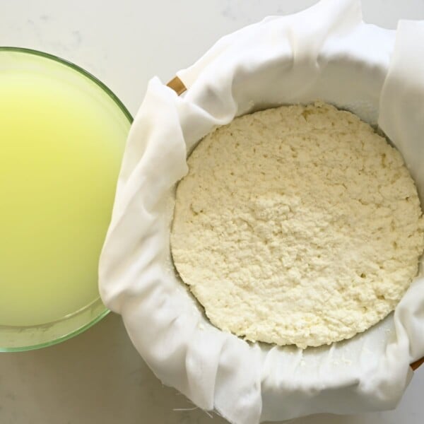 A bowl of whey and a bowl with drained milk curds.