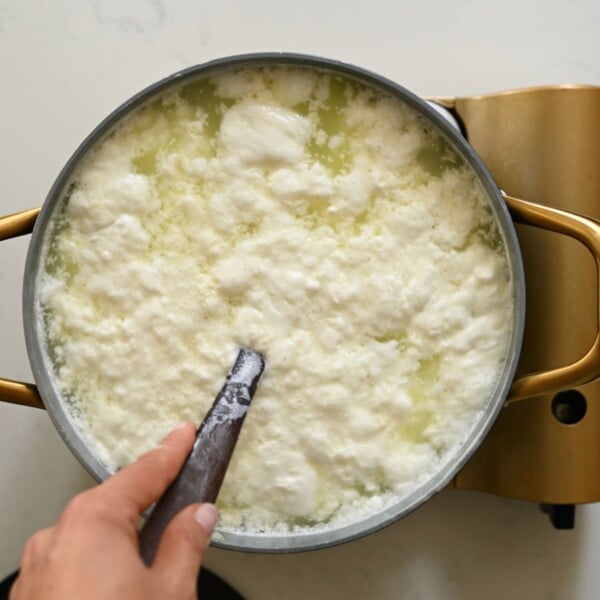 Milk curds separating from the whey in a large pot.