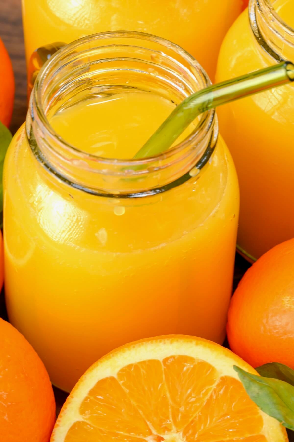 A glass filled with freshly squeezed orange juice and a glass straw.