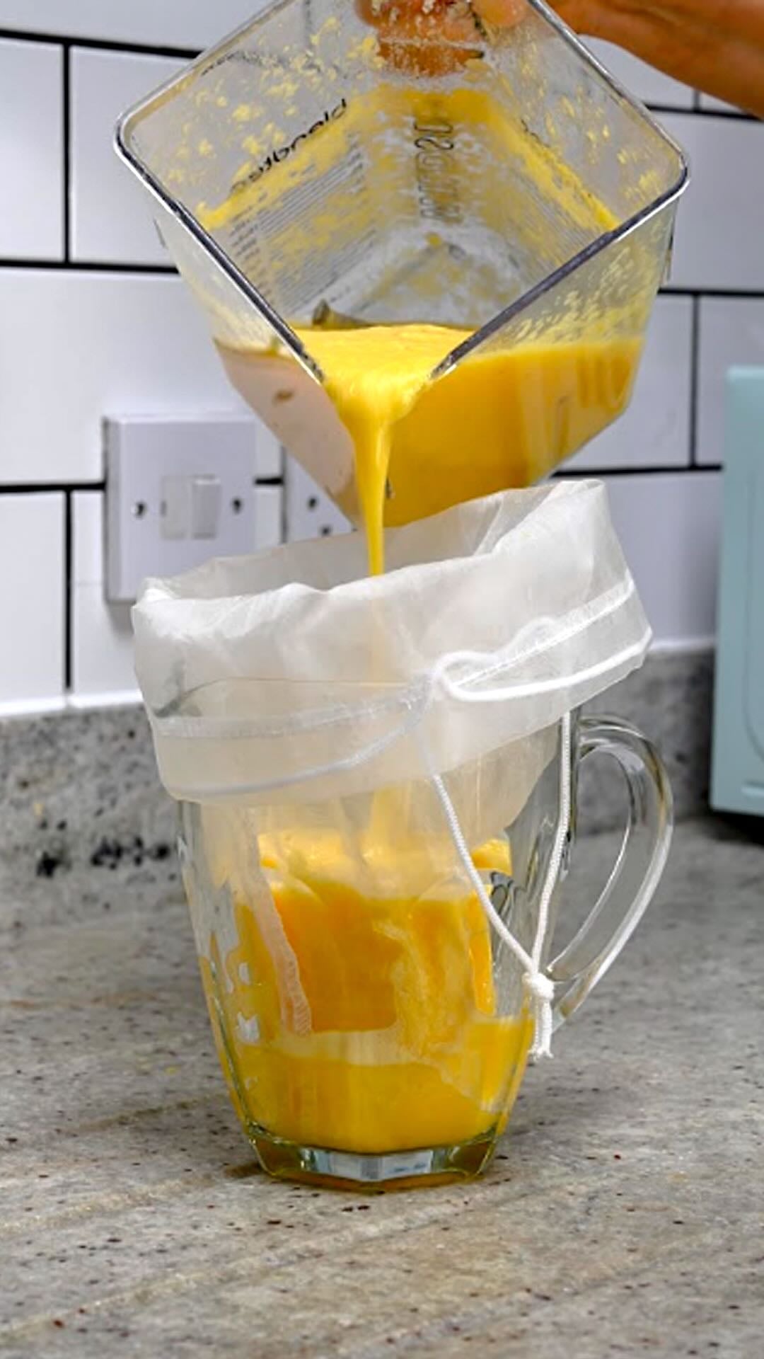 Pouring orange juice over a nutmilk bag.