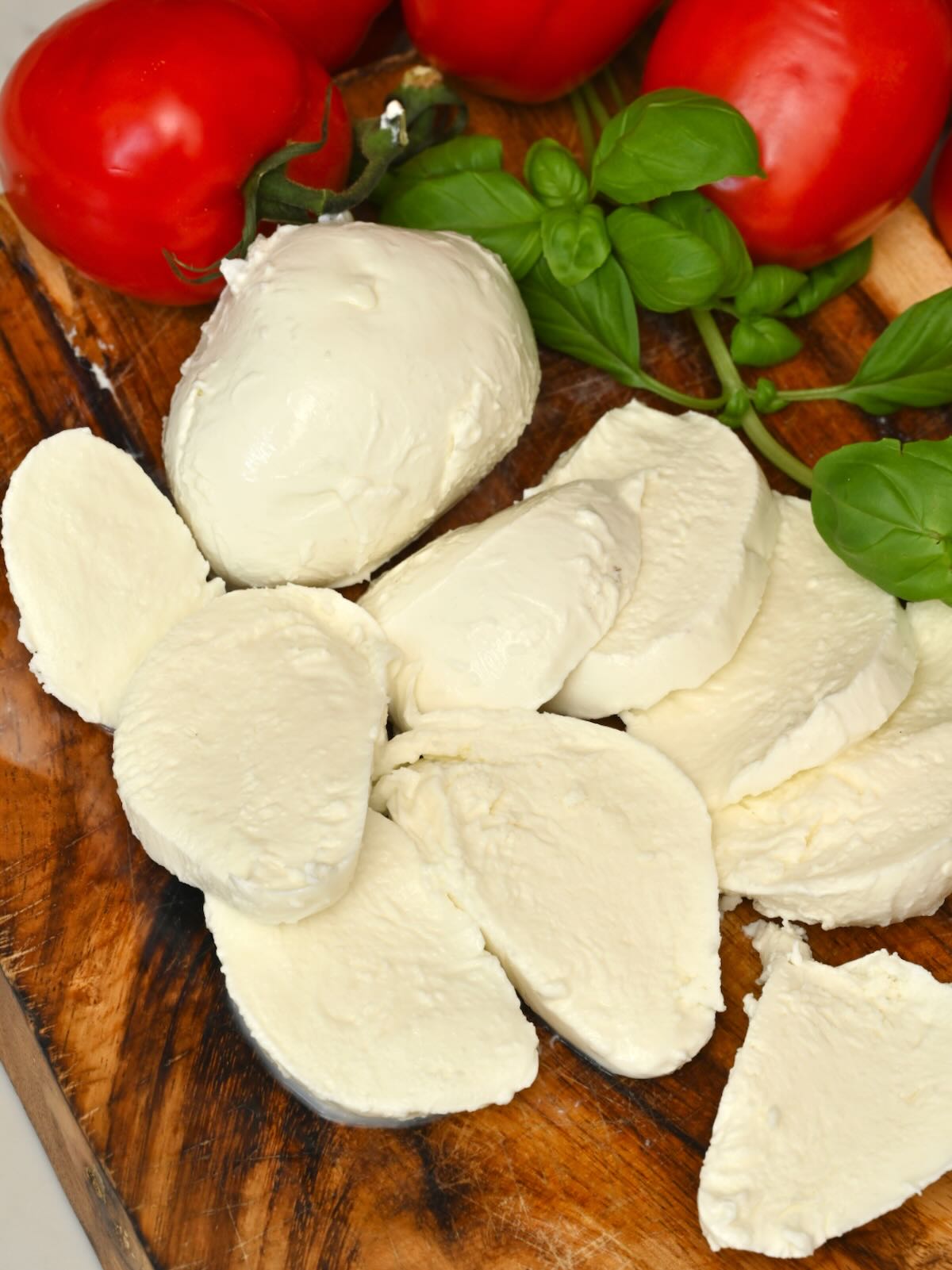 Homemade mozzarella cheese cut into slices with tomatoes and basil next to it.