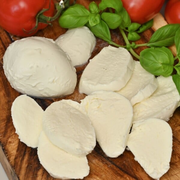 Homemade mozzarella cheese cut into slices with tomatoes and basil next to it.