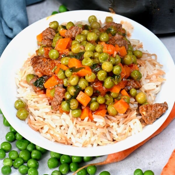 Bazella stew with beef, peas, and carrots served over vermicelli rice on a plate.