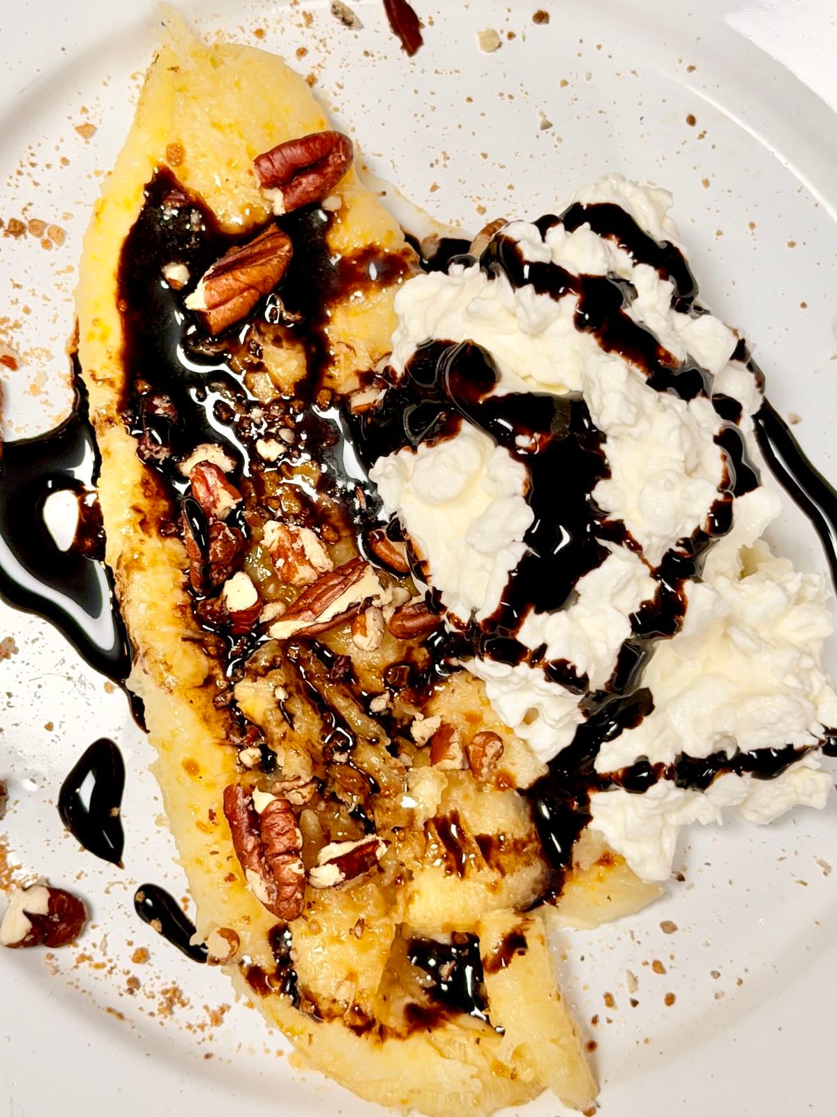 Caramelized banana topped with cottage cheese, toasted pecans, and a chocolate drizzle on a white plate.