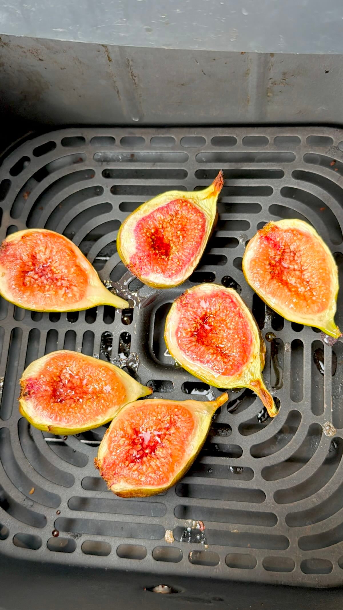 Halved figs, cut-side up, arranged in an air fryer basket after roasting.