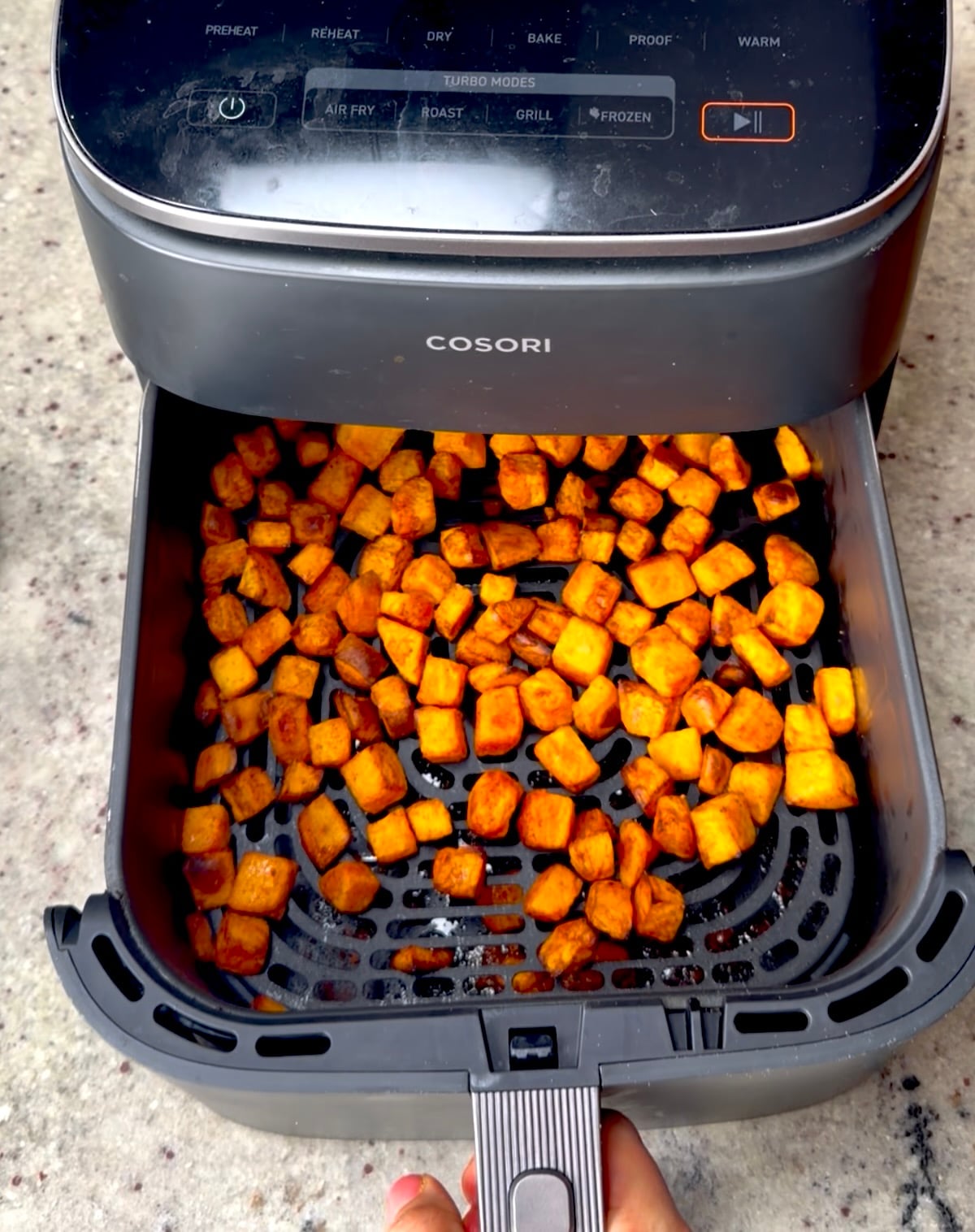Air fryer drawer pulled open to show roasted sweet potato cubes.