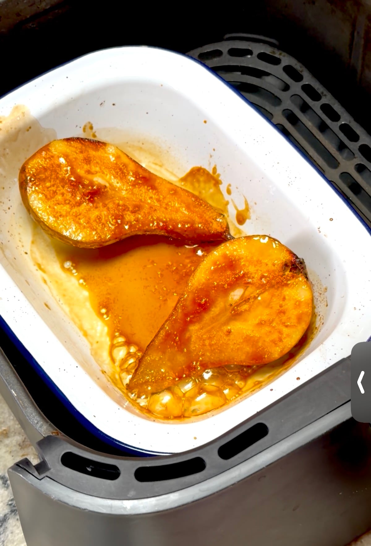 Pear slices caramelizing in an enamel dish with honey syrup inside an air fryer.