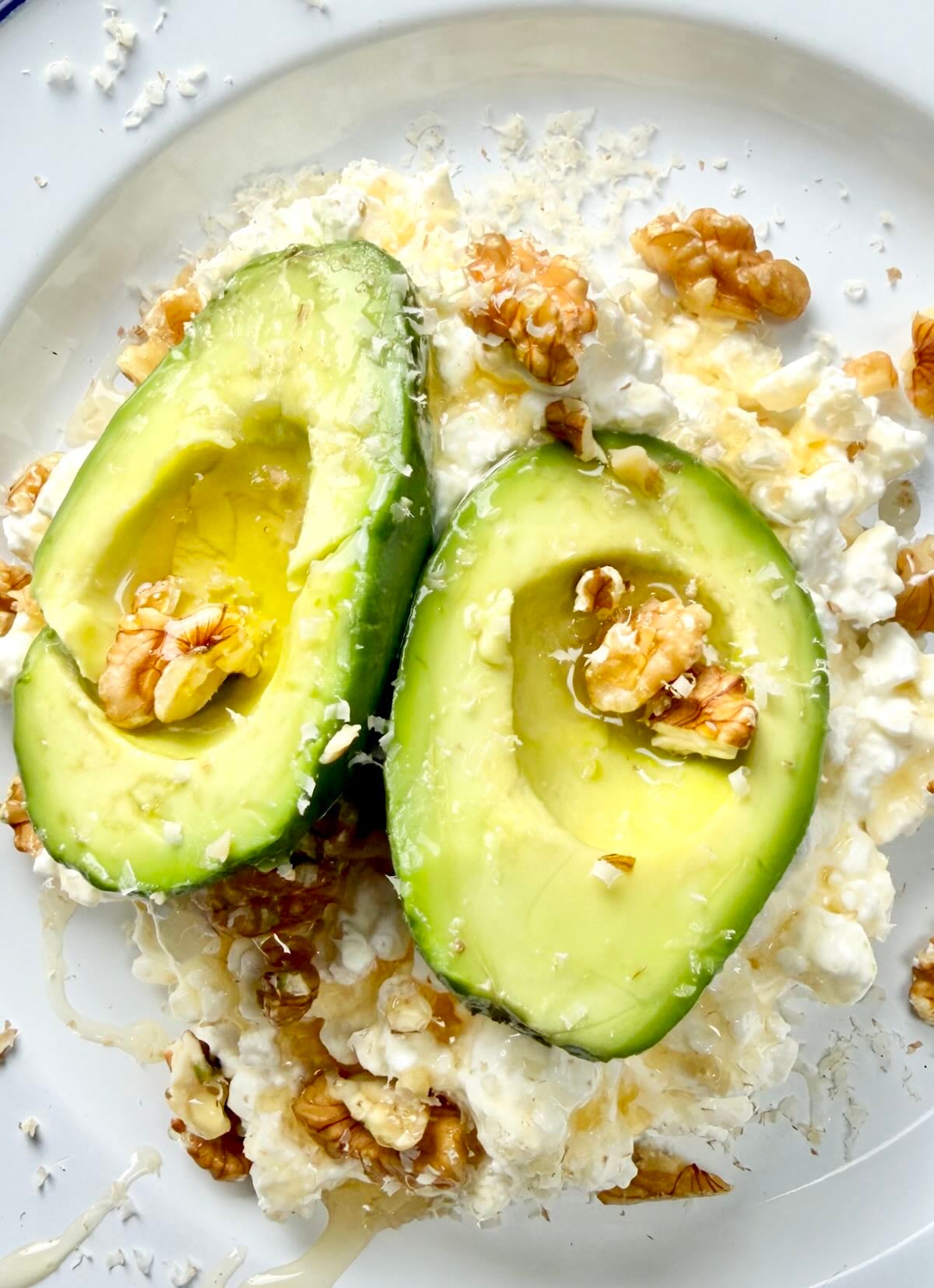 Cottage cheese bowl topped with avocado halves, walnuts and a drizzle of honey.