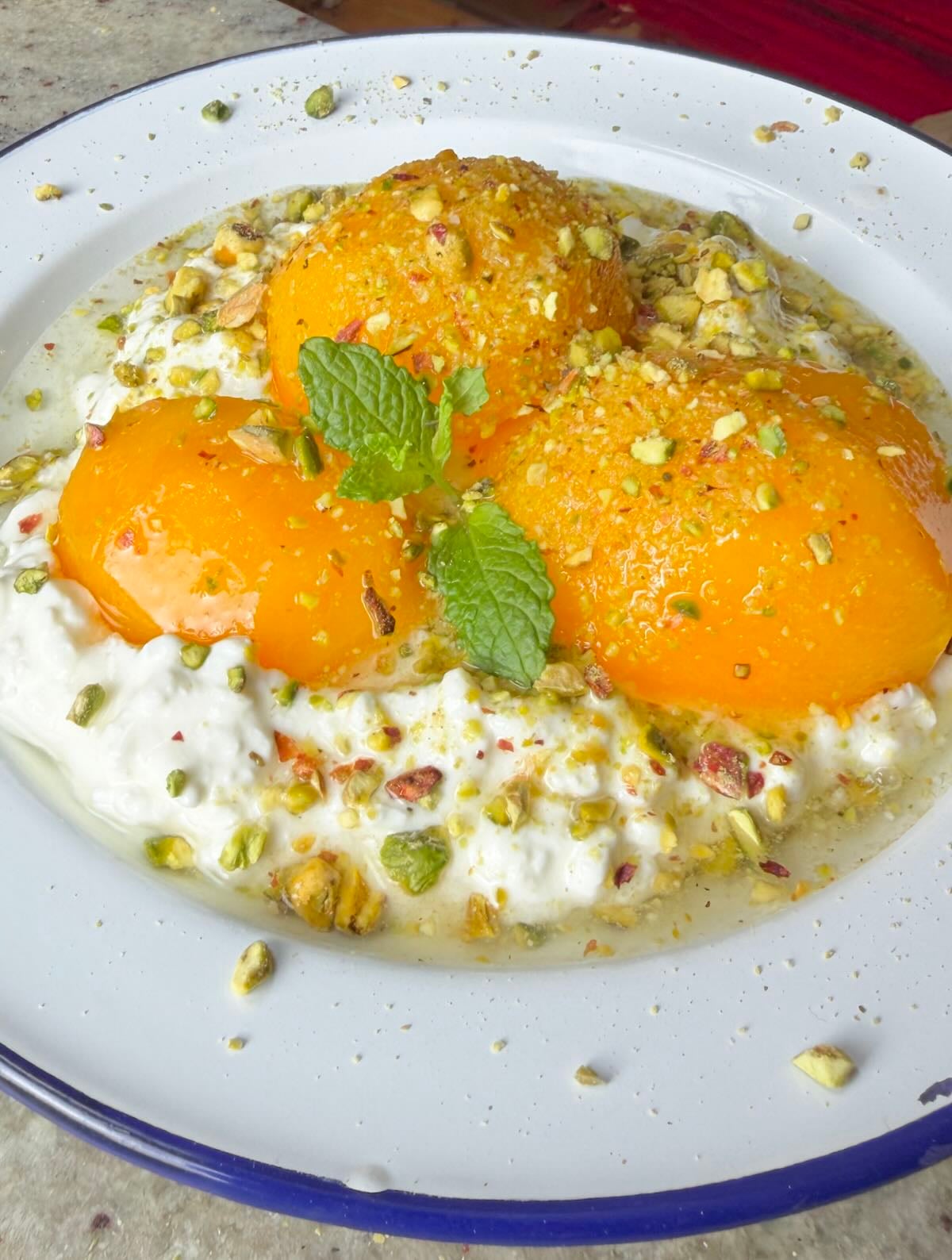 Cottage cheese topped with peach halves, crushed pistachios, and mint leaves.