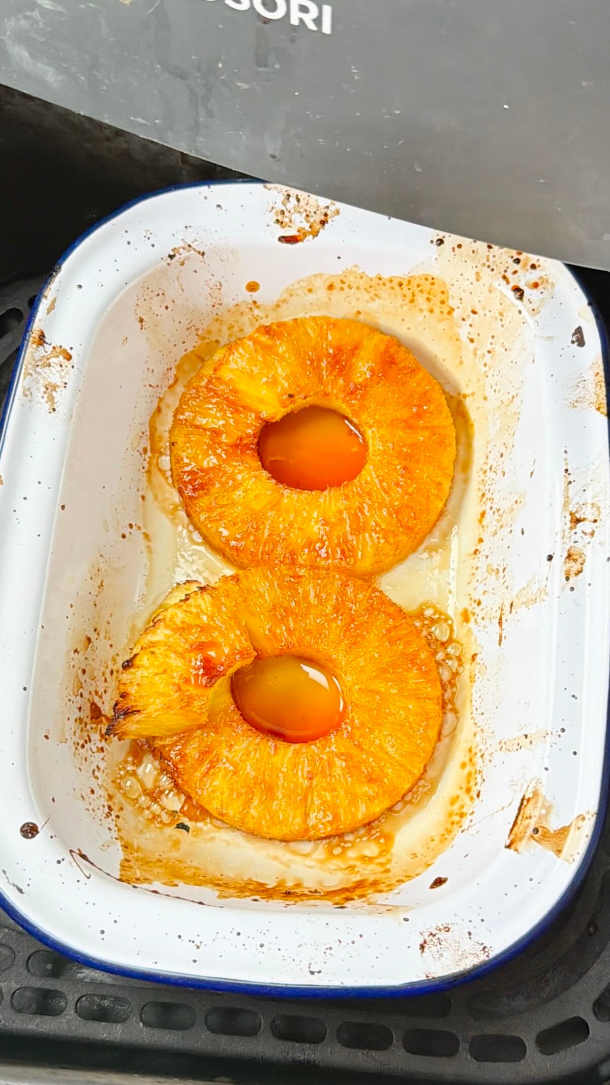 Pineapple rings caramelizing in an enamel dish in the air fryer with syrup bubbling around them.
