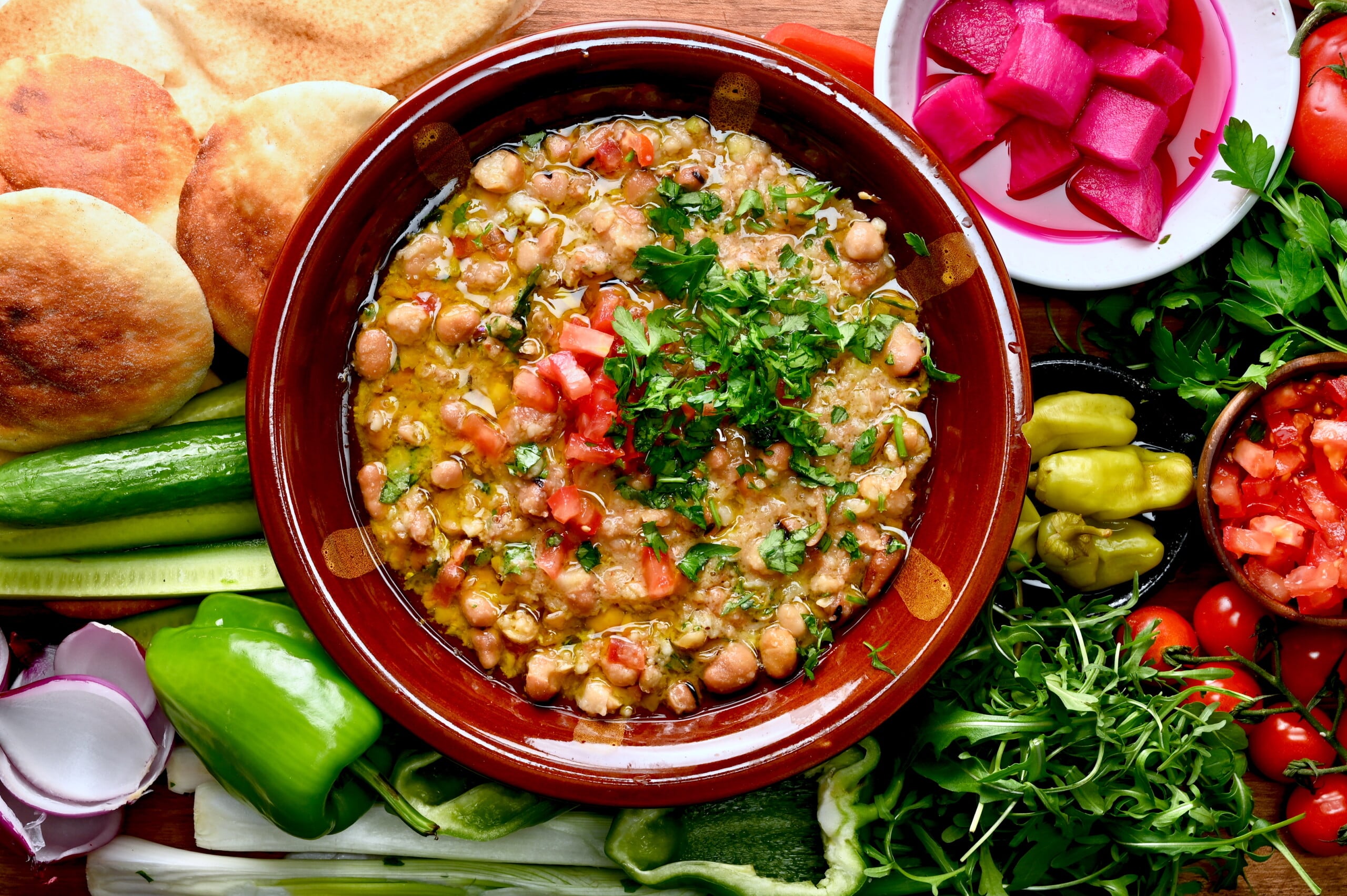 Ful medames served in a shallow bowl, topped with parsley and chopped tomatoes, with fresh sides.