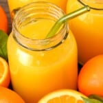 side view of mason jar of fresh orange juice with cut oranges on the side
