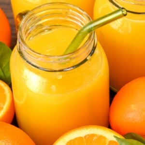 side view of mason jar of fresh orange juice with cut oranges on the side