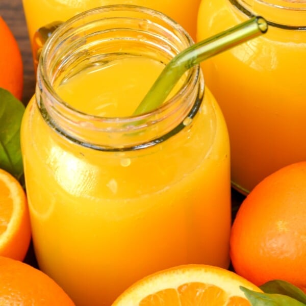 side view of mason jar of fresh orange juice with cut oranges on the side