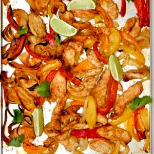 square photo of sheet pan of baked chicken strips, red and yellow peppers, and onions with lime wedges and cilantro.