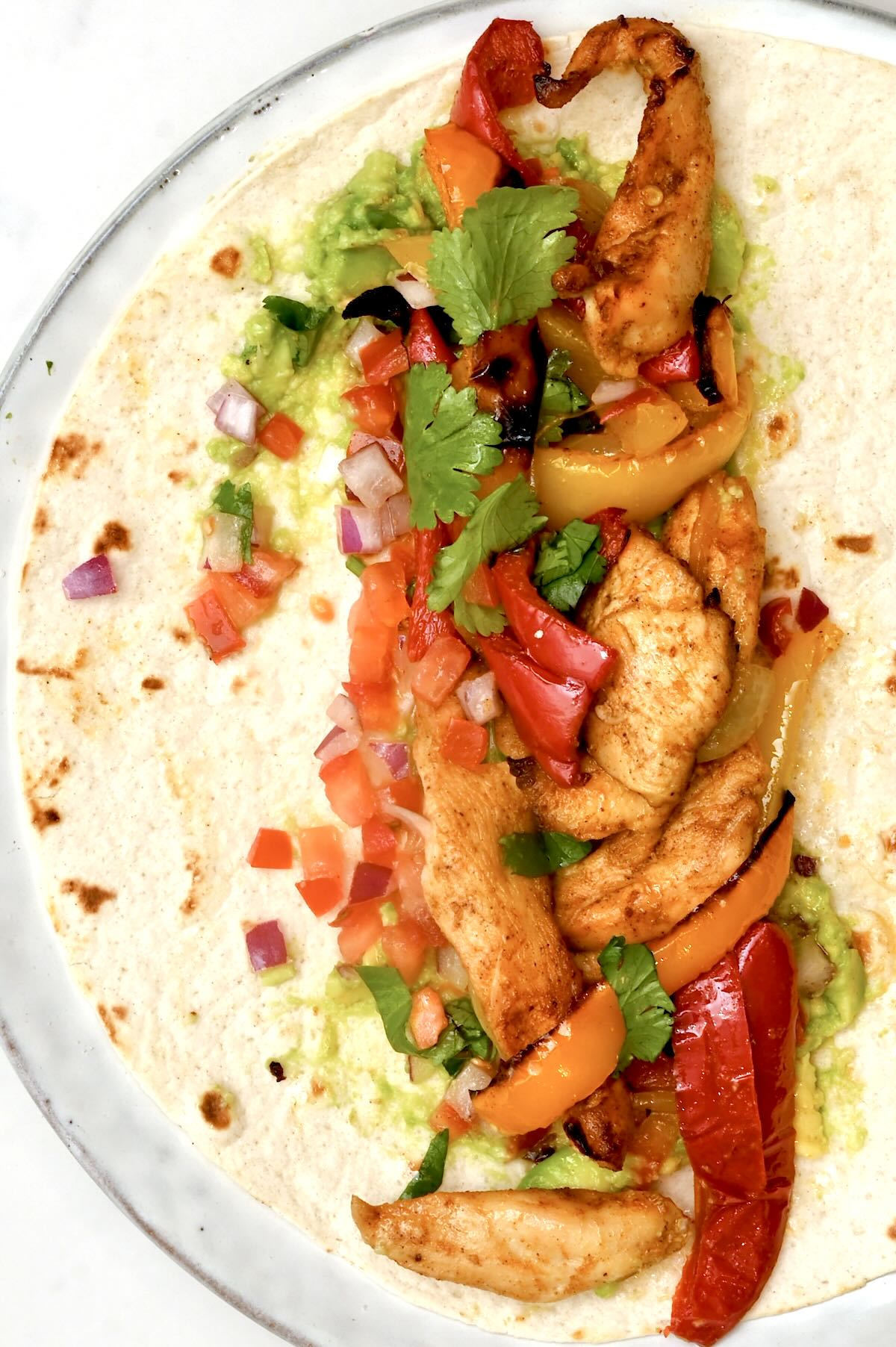 Close‑up chicken fajita on a flour tortilla with roasted peppers on a white plate