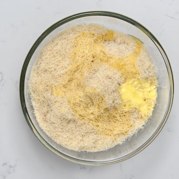 Kataifi mixed with melted butter in a bowl.
