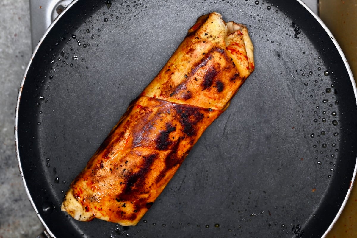 Crispy pan-grilled shawarma wrap with charred spots in a skillet.