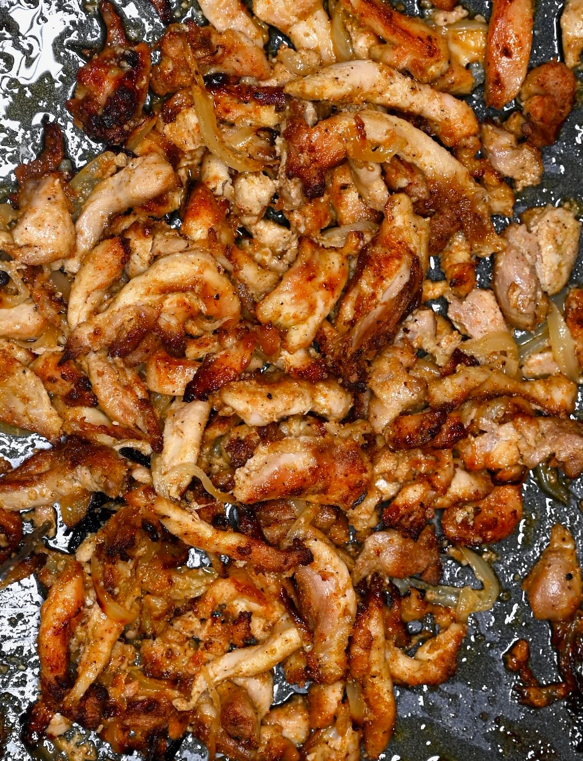 Close-up of chicken shawarma strips with caramelized onions and crispy edges on a pan.