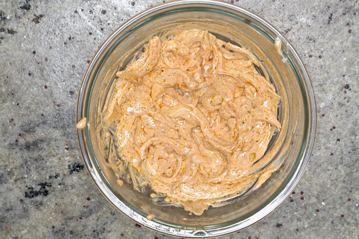 Shawarma yogurt marinade mixed with sliced onions in a glass bowl.