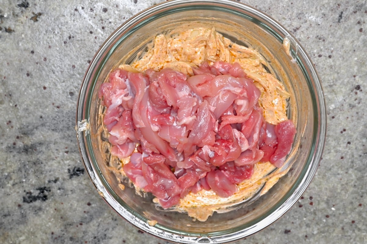 Raw chicken strips added to a bowl of shawarma yogurt marinade.